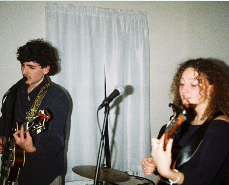 Audrey playing guitar indoors with a bandmate